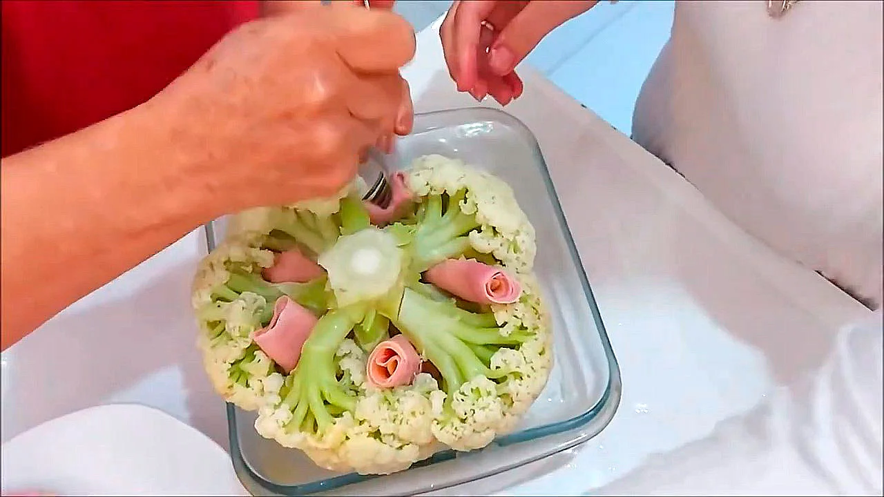 Travessa com couve-flor inteira, coberta de molho branco dourado e parmesão, corte mostrando rolinhos de presunto e queijo entre os buquês;