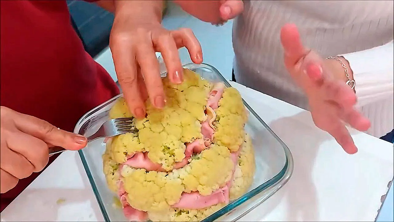Couve-flor inteira recheada com presunto e queijo. Travessa com couve-flor inteira, coberta de molho branco dourado e parmesão, corte mostrando rolinhos de presunto e queijo entre os buquês;